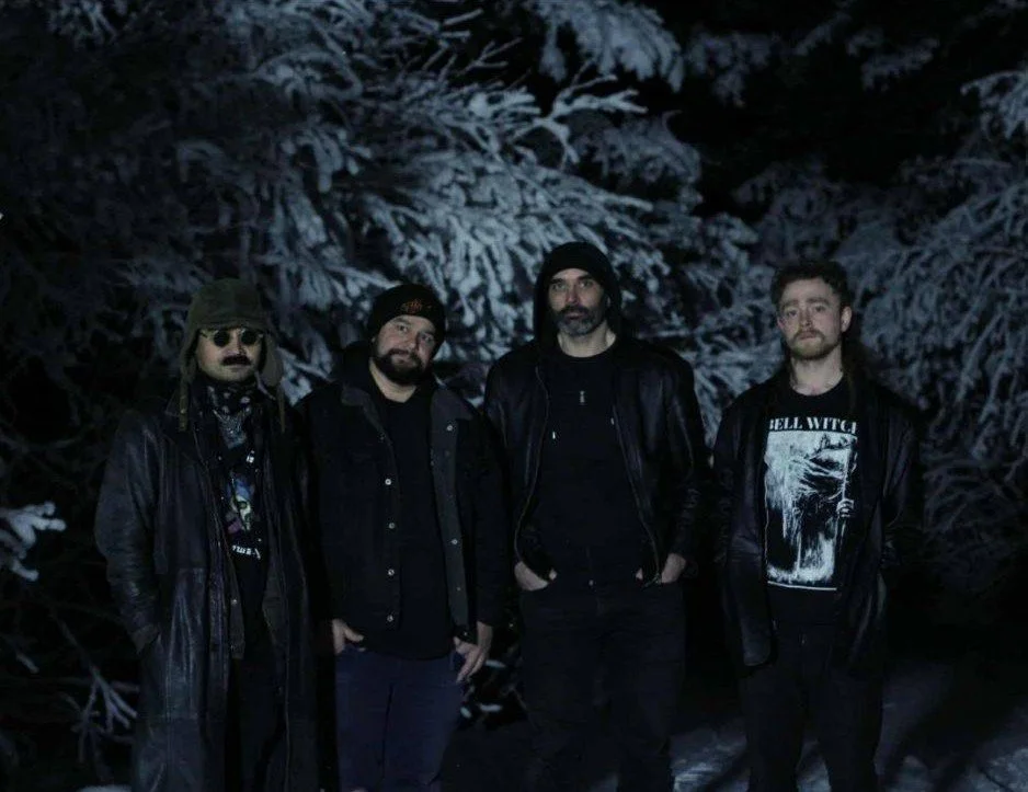 Four men standing outdoors in a snowy forest at night.