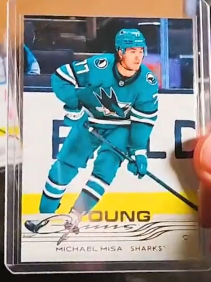 A hockey trading card featuring a player in a teal San Jose Sharks uniform, wearing a helmet and holding a hockey stick on the ice rink.
