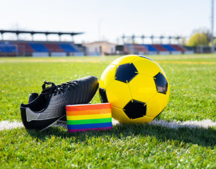 A yellow and black soccer ball, a black sports bag, and a rainbow-colored wristband on a green grass field at a stadium.