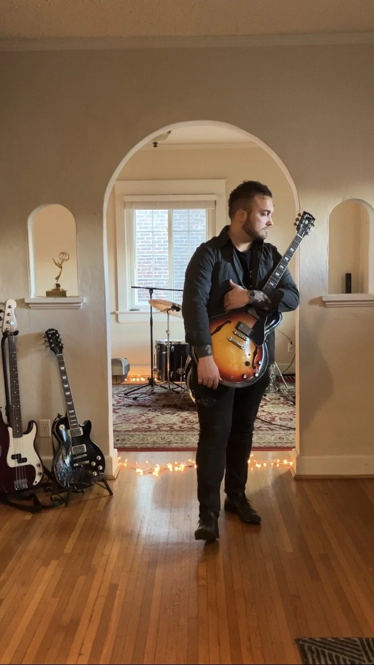 Jacob Diddens with his 2018 Gibson ES 335 standing in the entrance of Big Cat Recordings. Big Cat Recordings LLC is decorated with string lights, multiple, high-fidelity instruments, and more.