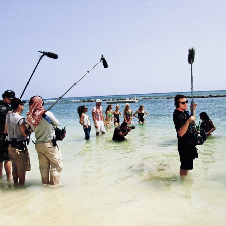 Film crew filming people in shallow ocean water at beach.