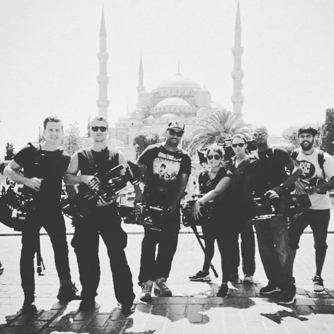 Group of seven people standing in front of a mosque with minarets, some holding cameras, in black and white