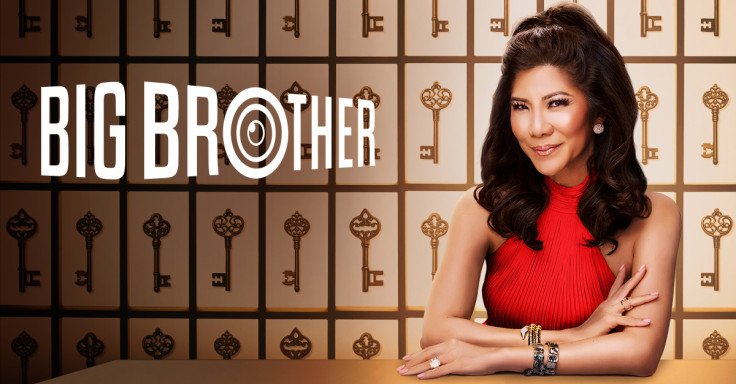 A woman in a red sleeveless top sitting with her arms crossed in front of her, smiling slightly. Behind her is a wall decorated with large gold and black keys. To the left, the logo for Big Brother reality TV show is displayed.