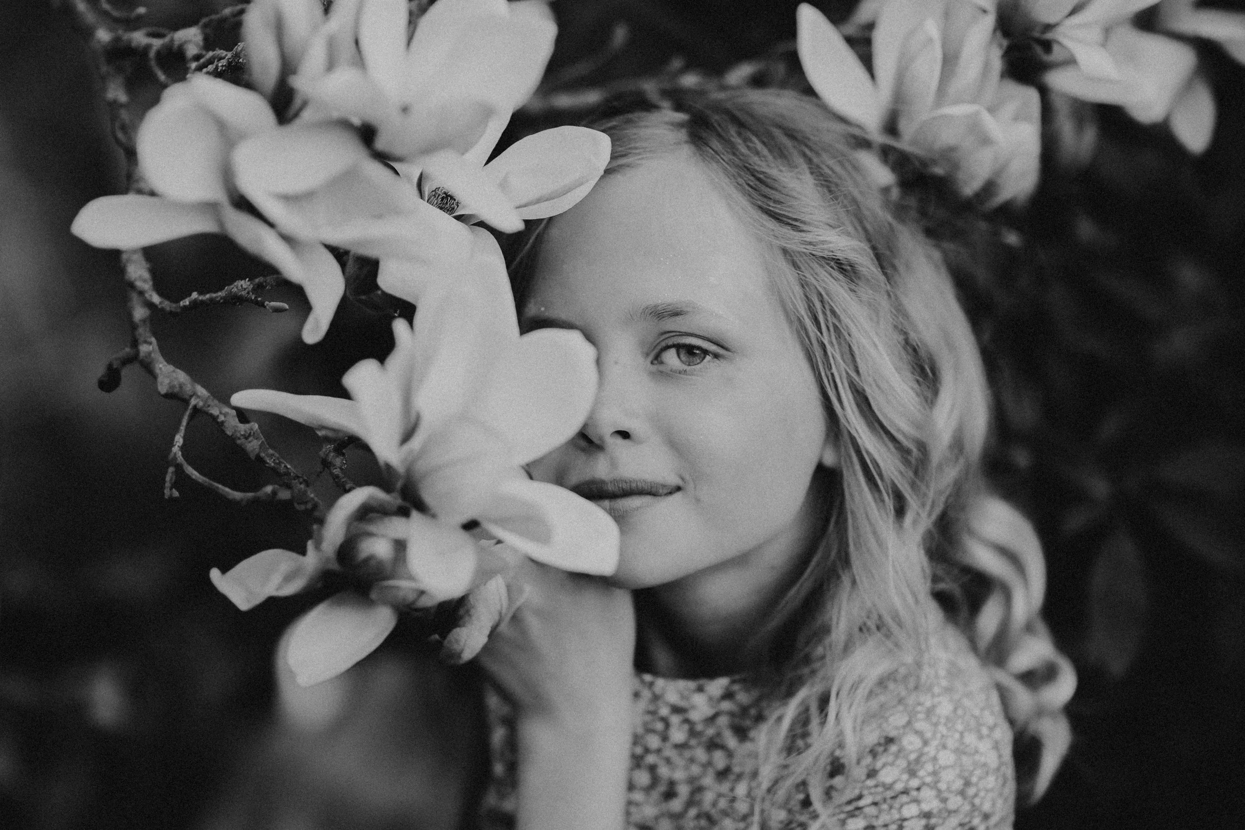 Junge Frau mit langem, gewelltem Haar, halb verdeckt hinter Blumen, in schwarzen und weißen Tönen, nahaufnahme