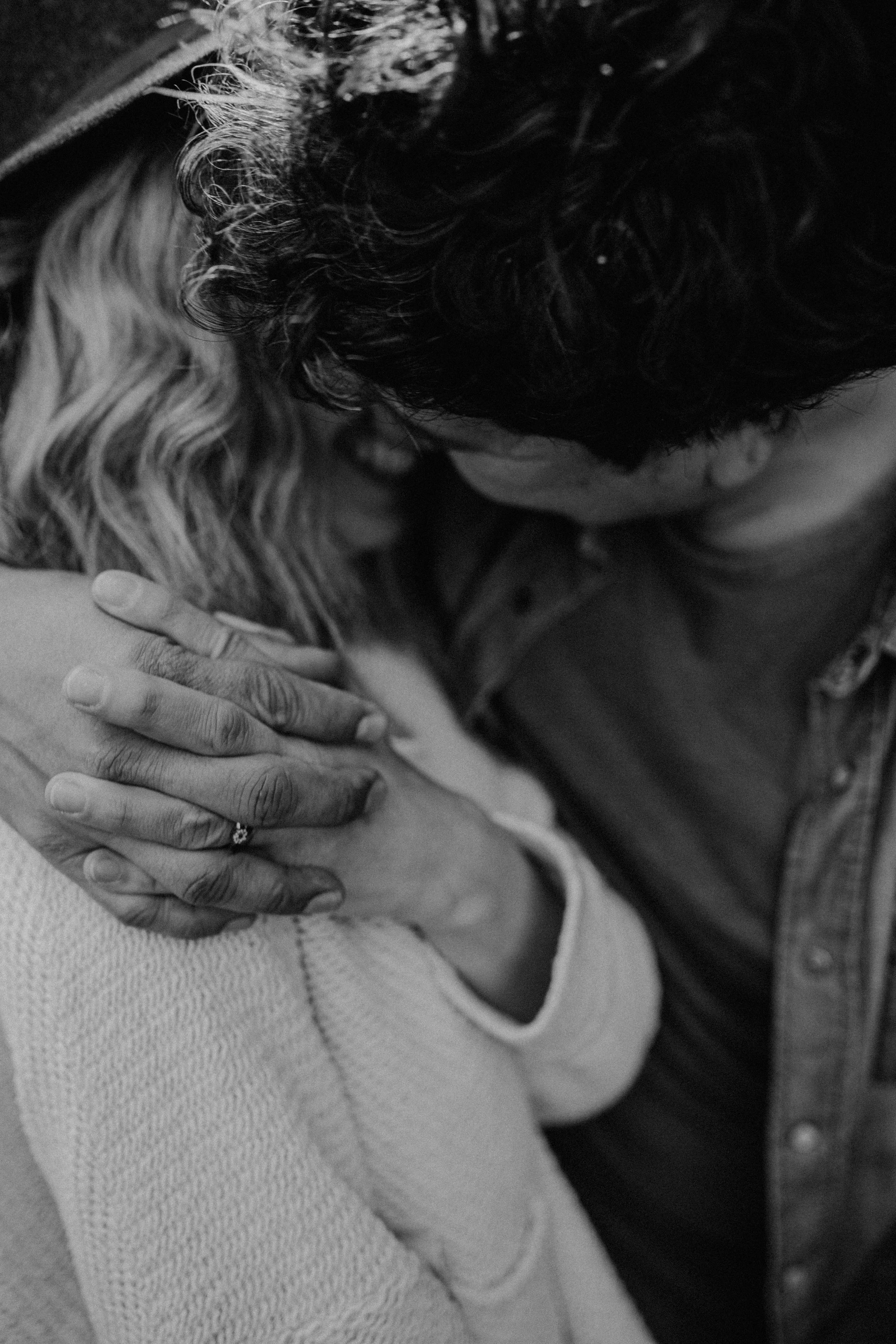 Ein Mensch umarmt einen Hund liebevoll. Der Mensch trägt ein Trägertop und einen Ring an der Hand. Das Bild ist in Schwarz-Weiß gehalten.