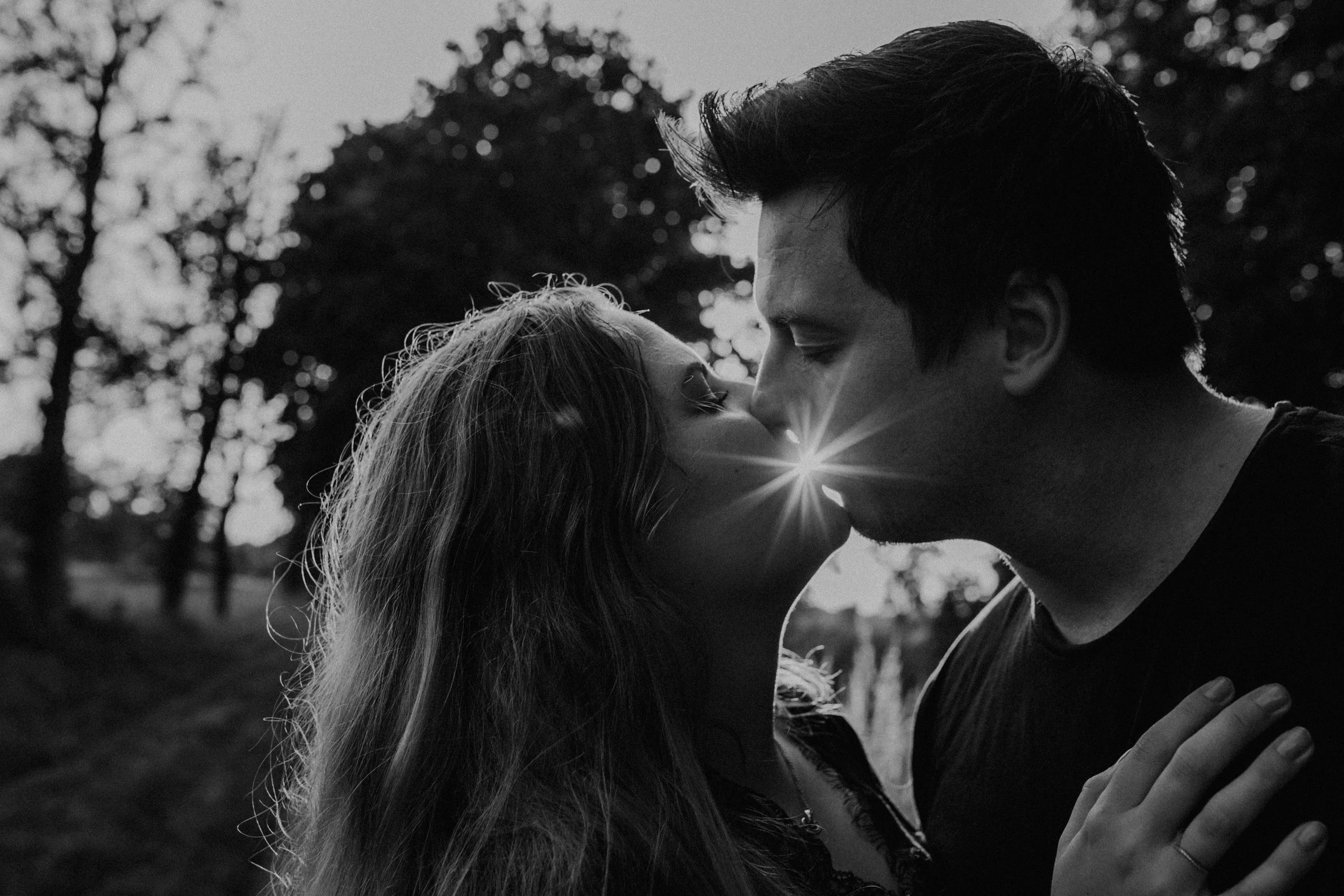 Ein Paar küsst sich im Freien bei Sonnenuntergang, das Licht geht durch ihre Gesichter.