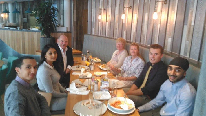 Seven people sitting around a restaurant table enjoying a meal together.