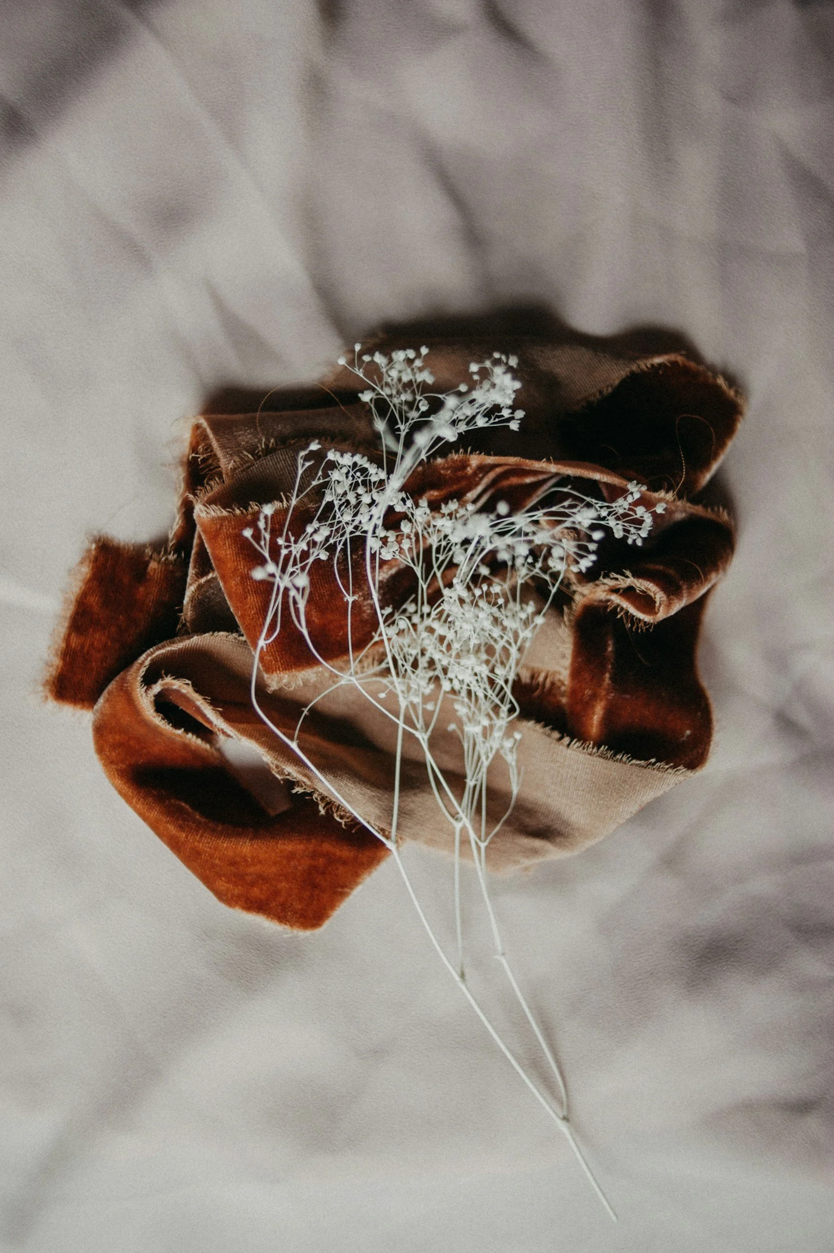 A brown velvet scrunchie with white baby's breath flowers on a soft fabric background.