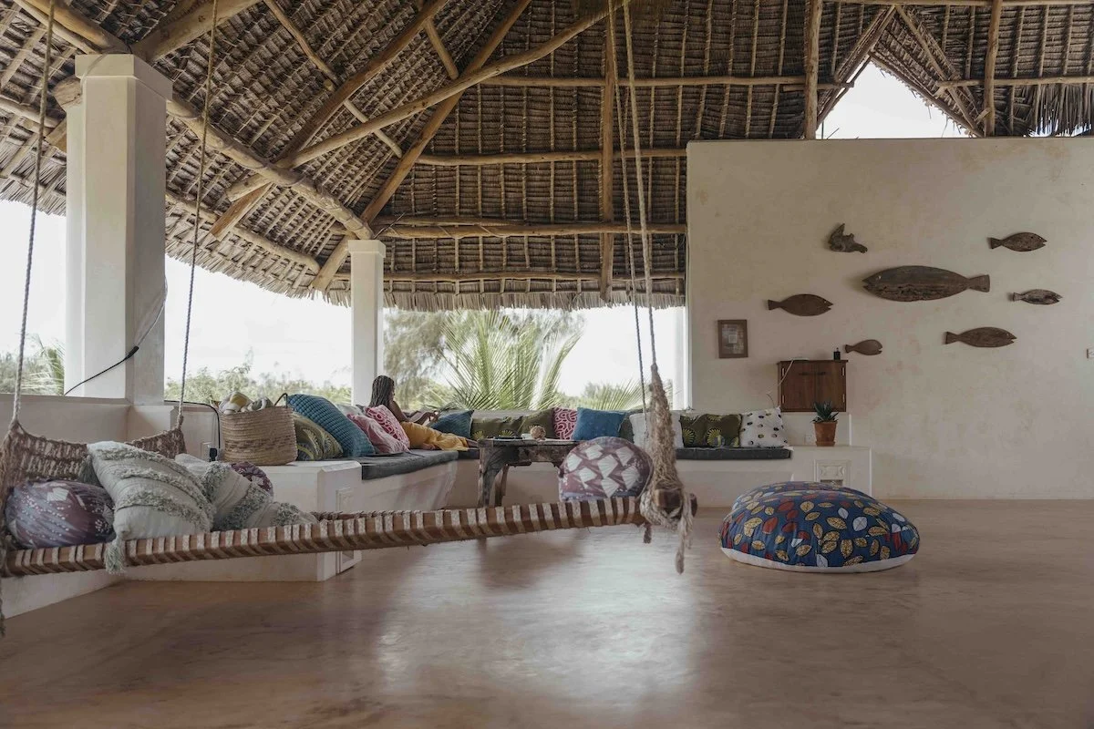 A woman lounging on the rooftop with lots of comfy cushions and palm thatched roof