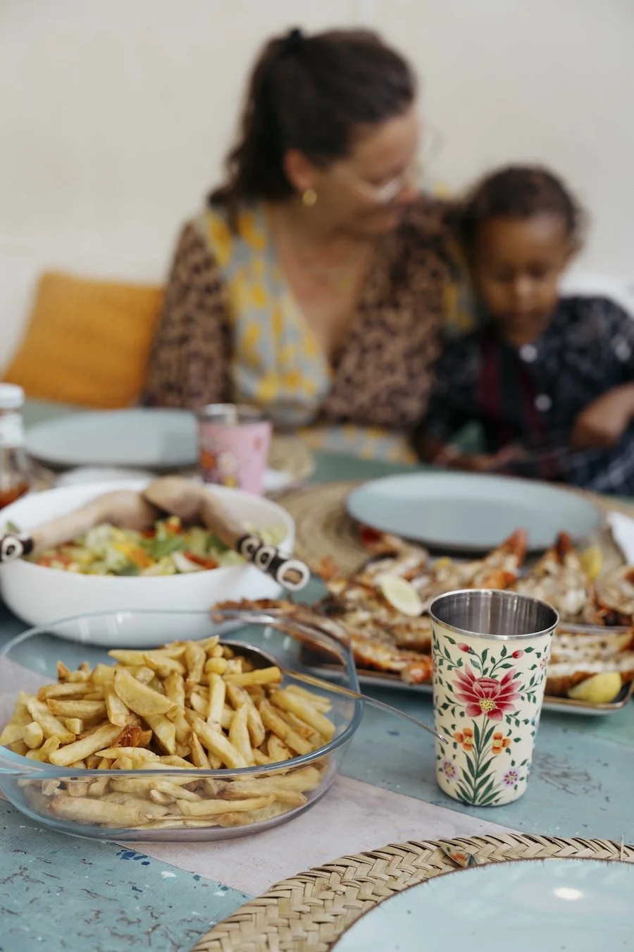 A full spread on a table of fresh lobster, chips and seasonal vegetables prepared by Chef Lawrence, with a mother and child sat in the background