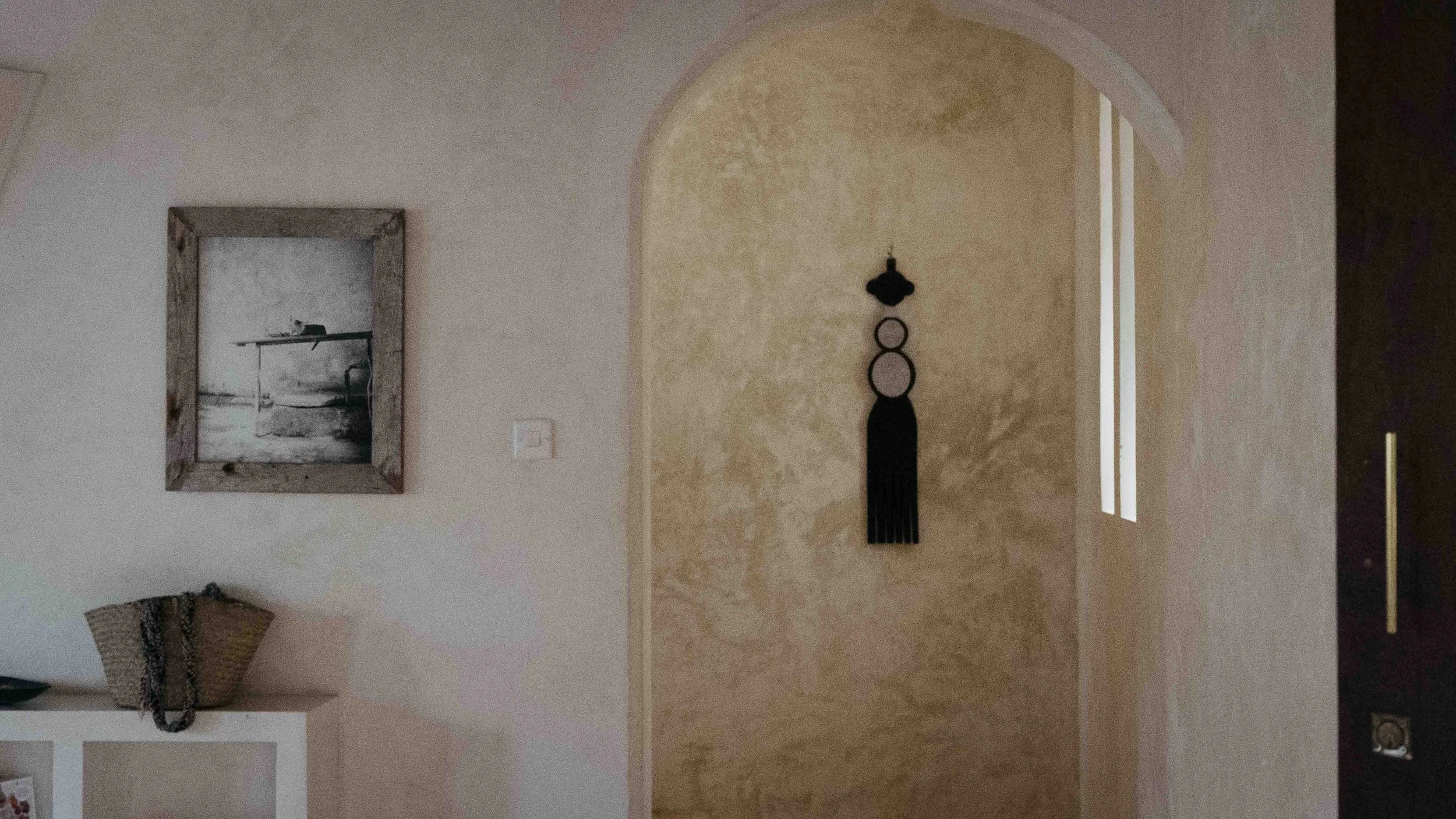 A built in bookshelf with a photograph of a cat hanging aboce with an elegant archway framing a traditional Central African art piece.