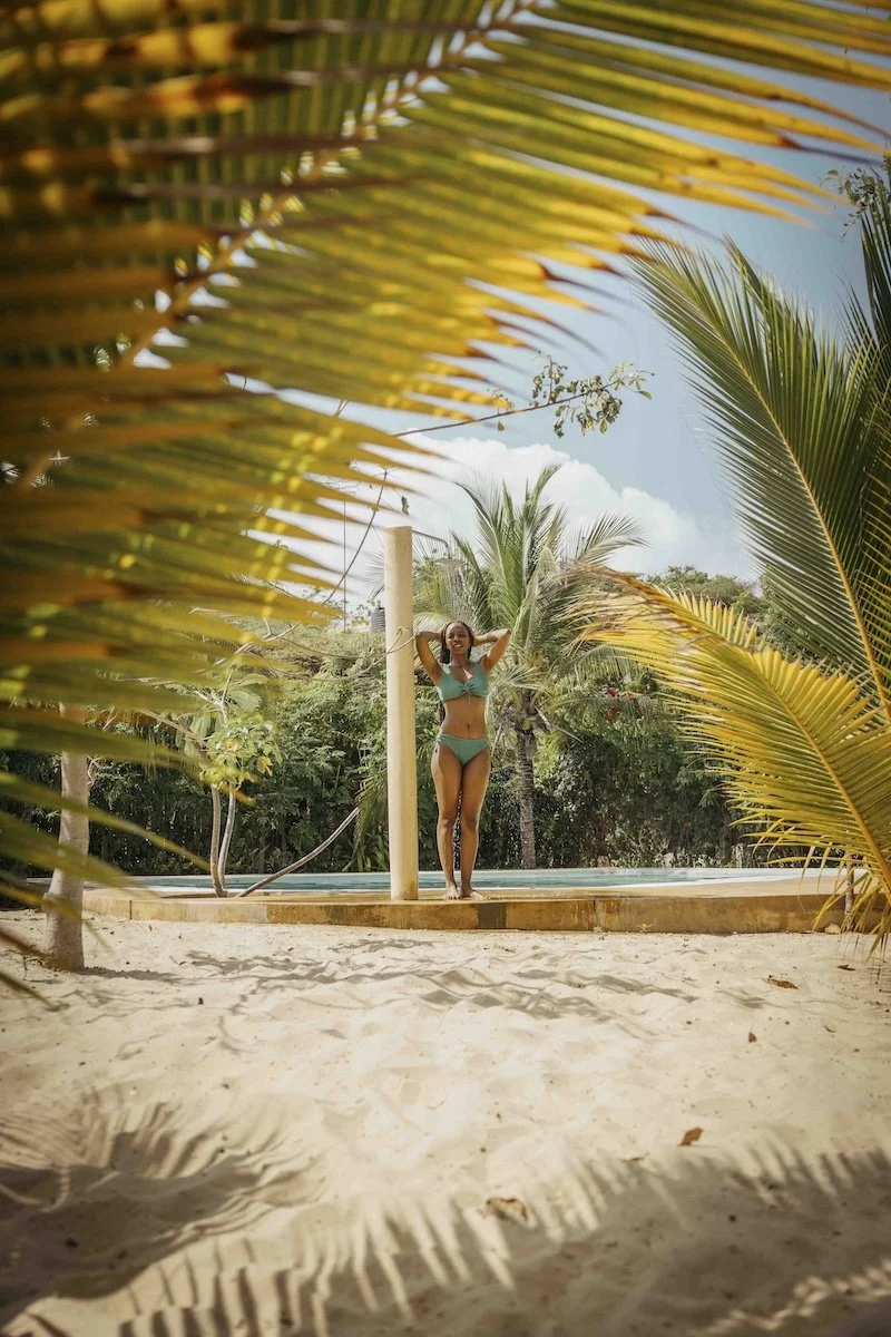 this shows palm trees and a woman showering under the pool shower in the garden