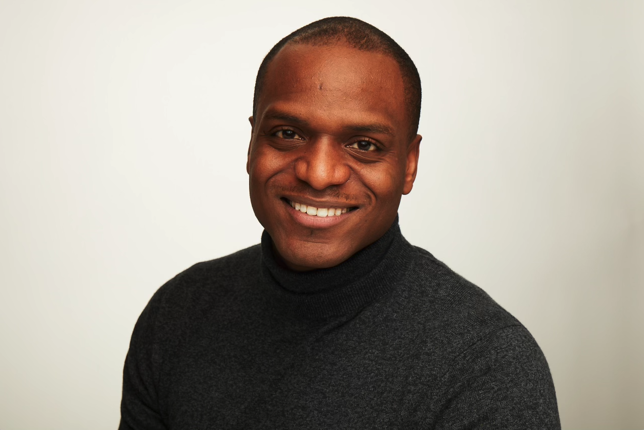 Portrait of a smiling man with short hair wearing a black turtleneck sweater against a plain light background.