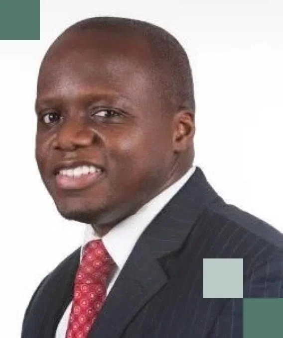 Portrait of a smiling man in a dark suit with a red patterned tie, white shirt, and a light-colored background.