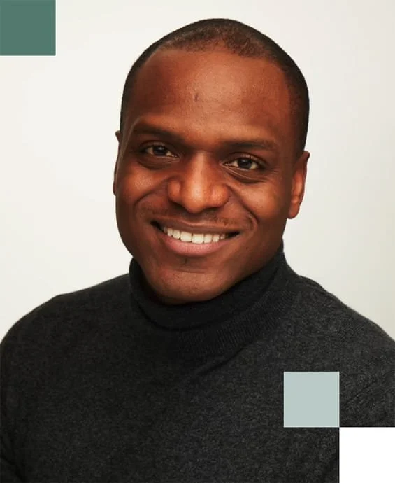 A smiling man with short hair wearing a black turtleneck against a plain light background.