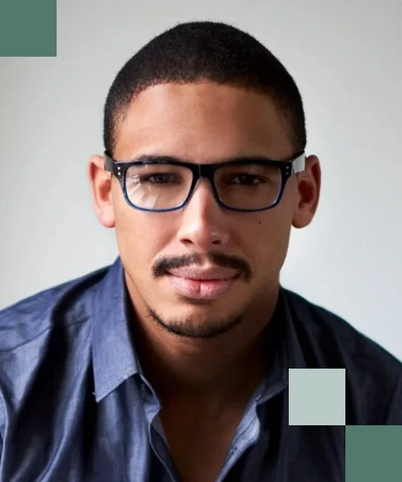 Portrait of a young man with short hair, glasses, and a goatee, wearing a blue collared shirt, looking at the camera.