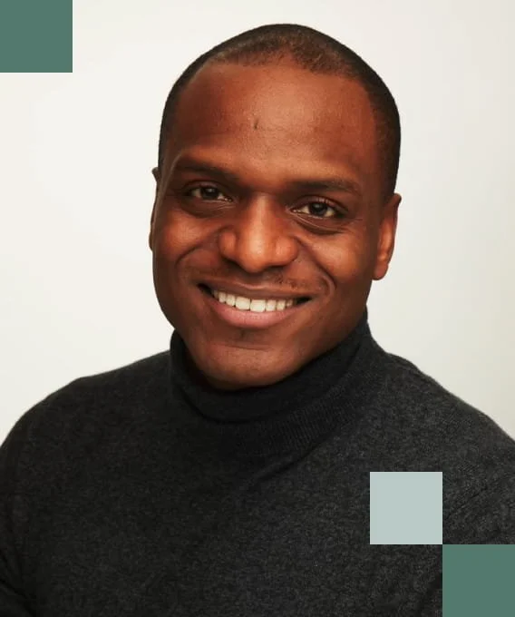 A smiling man with short hair wearing a black turtleneck sweater, posing against a plain white background.