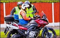 A police officer and a woman sitting on a red motorcycle near a red fence.