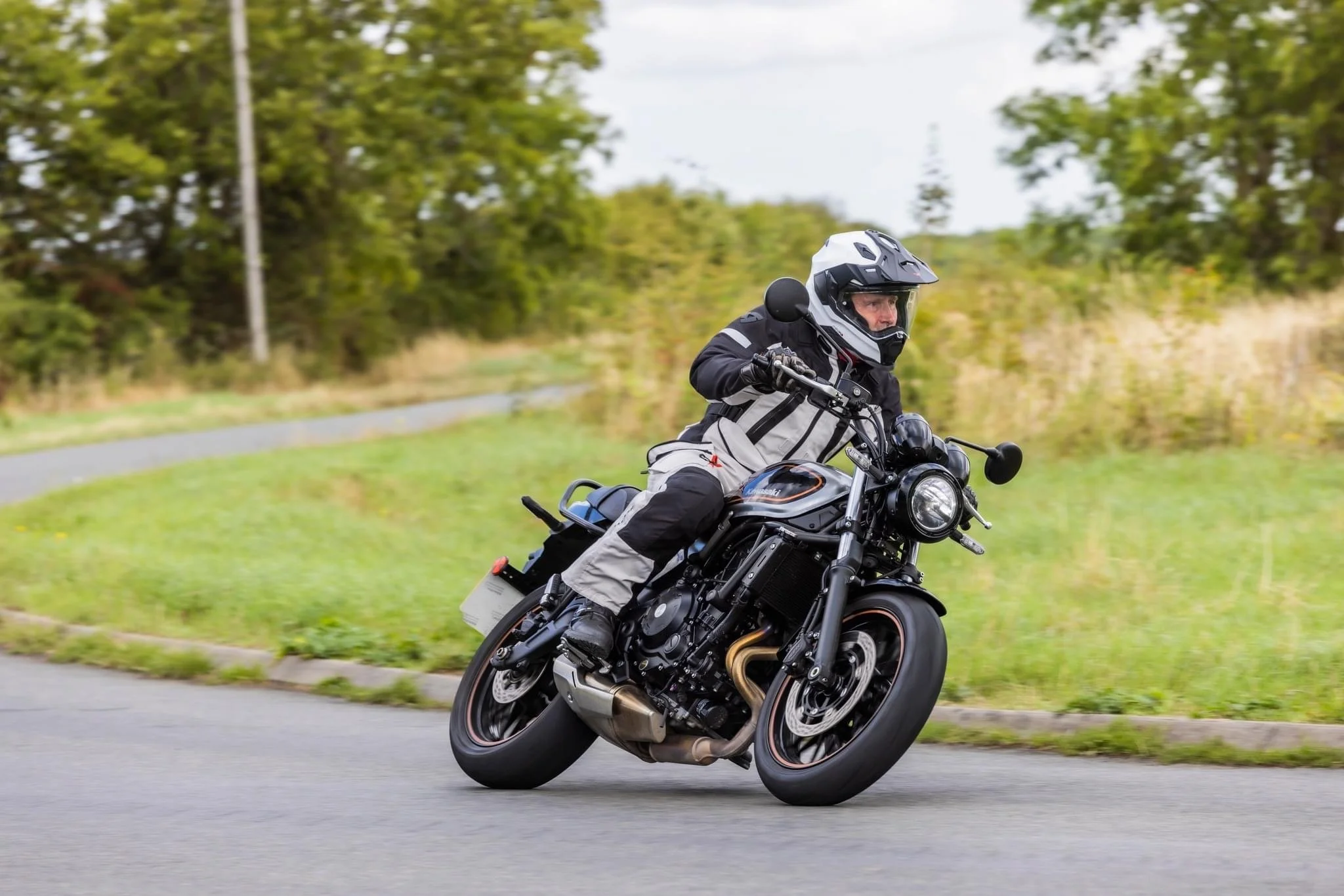 A person riding a black motorcycle on a curved road with green trees and grass in the background during daytime.