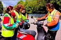 Three police officers in high-visibility vests are talking to a motorcyclist while they are standing next to a red motorcycle on a sunny day.