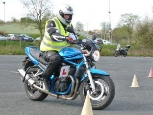 Motorcycle rider in a neon vest and helmet practicing riding skills around cones
