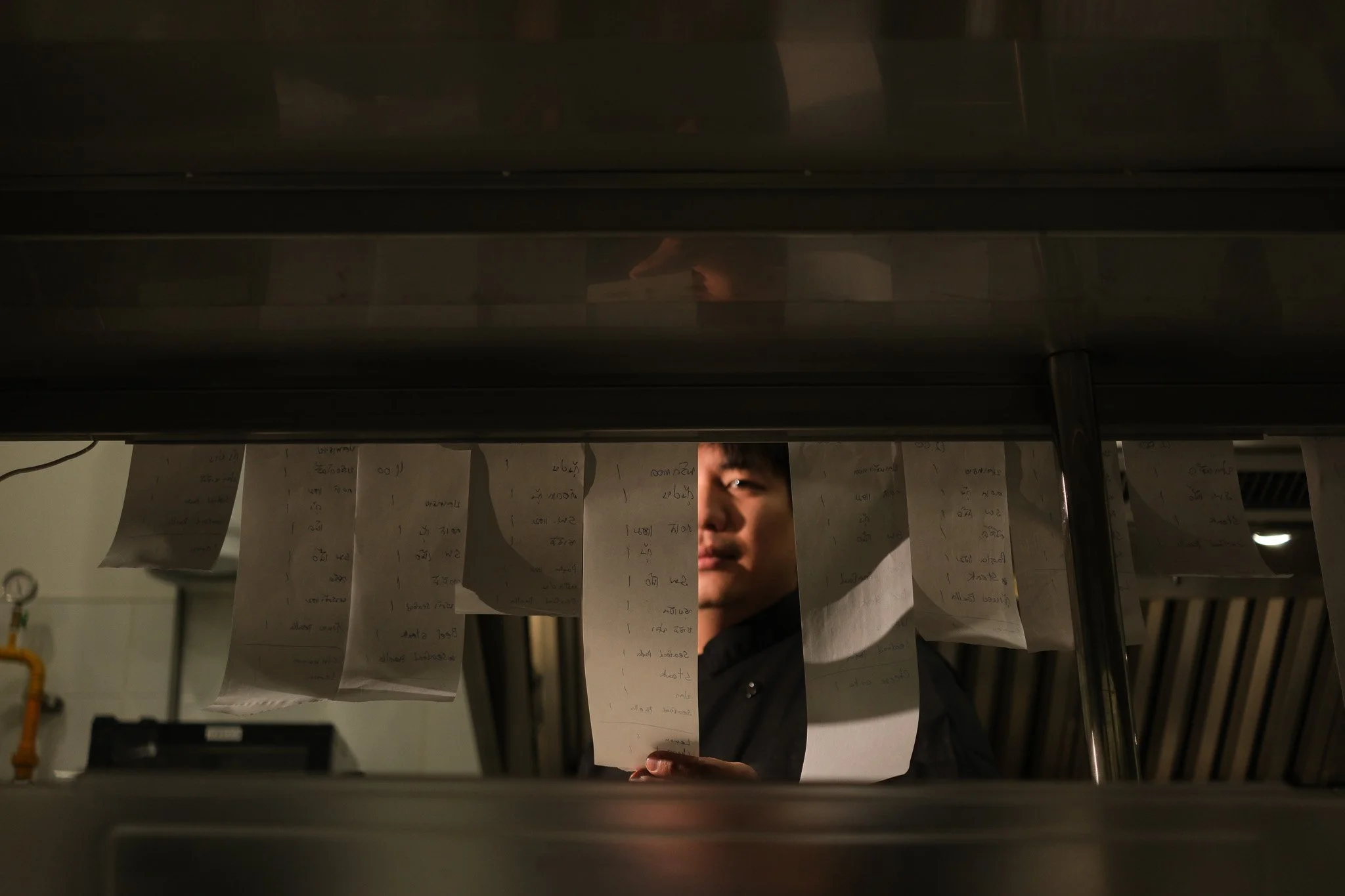 A person looking at food order tickets hanging inside a kitchen window.