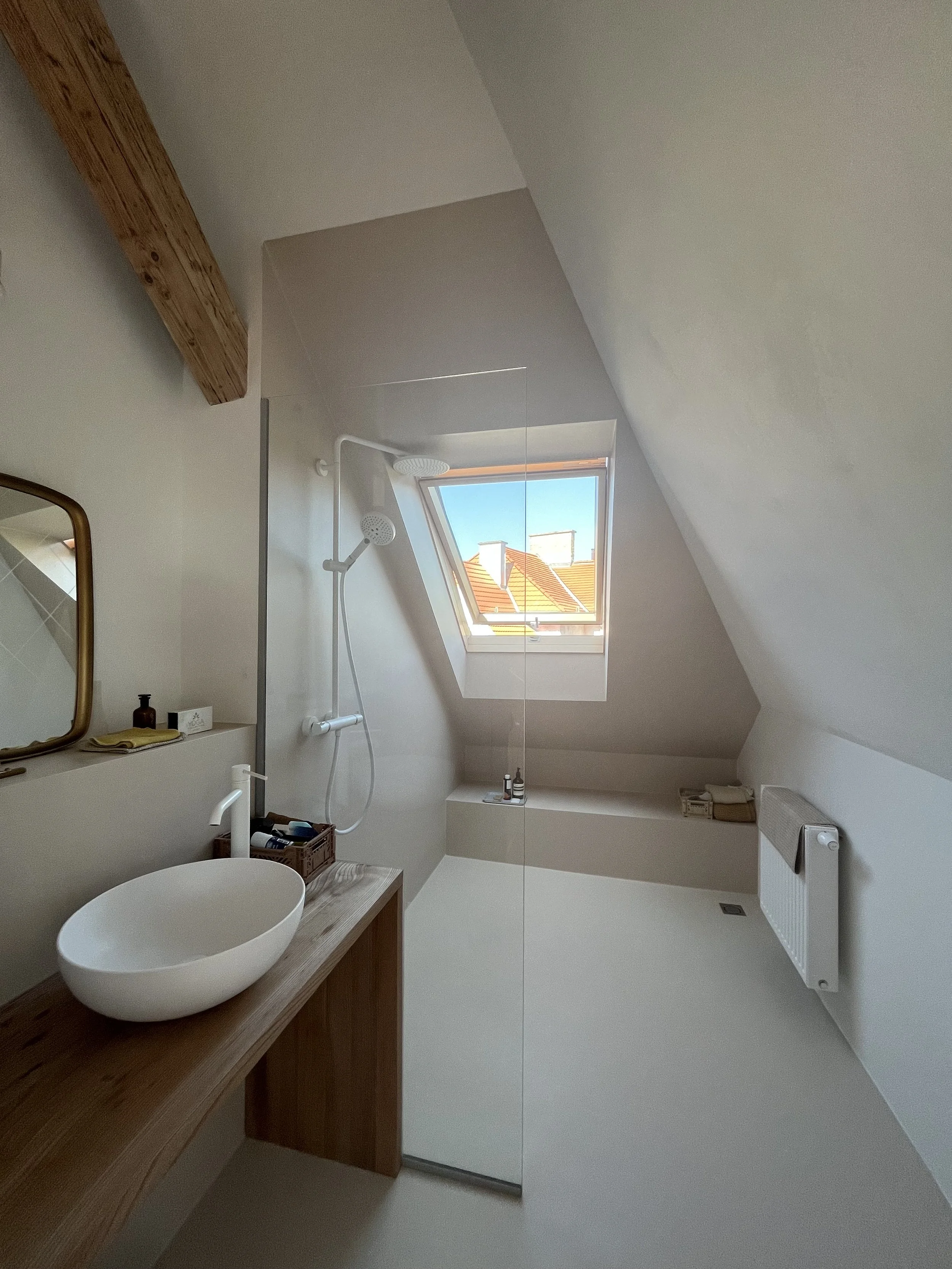 Ein kleines Badezimmer mit Schrägdach, einer kleinen Badewanne, einem Dachfenster und einer Waschtisch mit Schüsselwaschbecken.