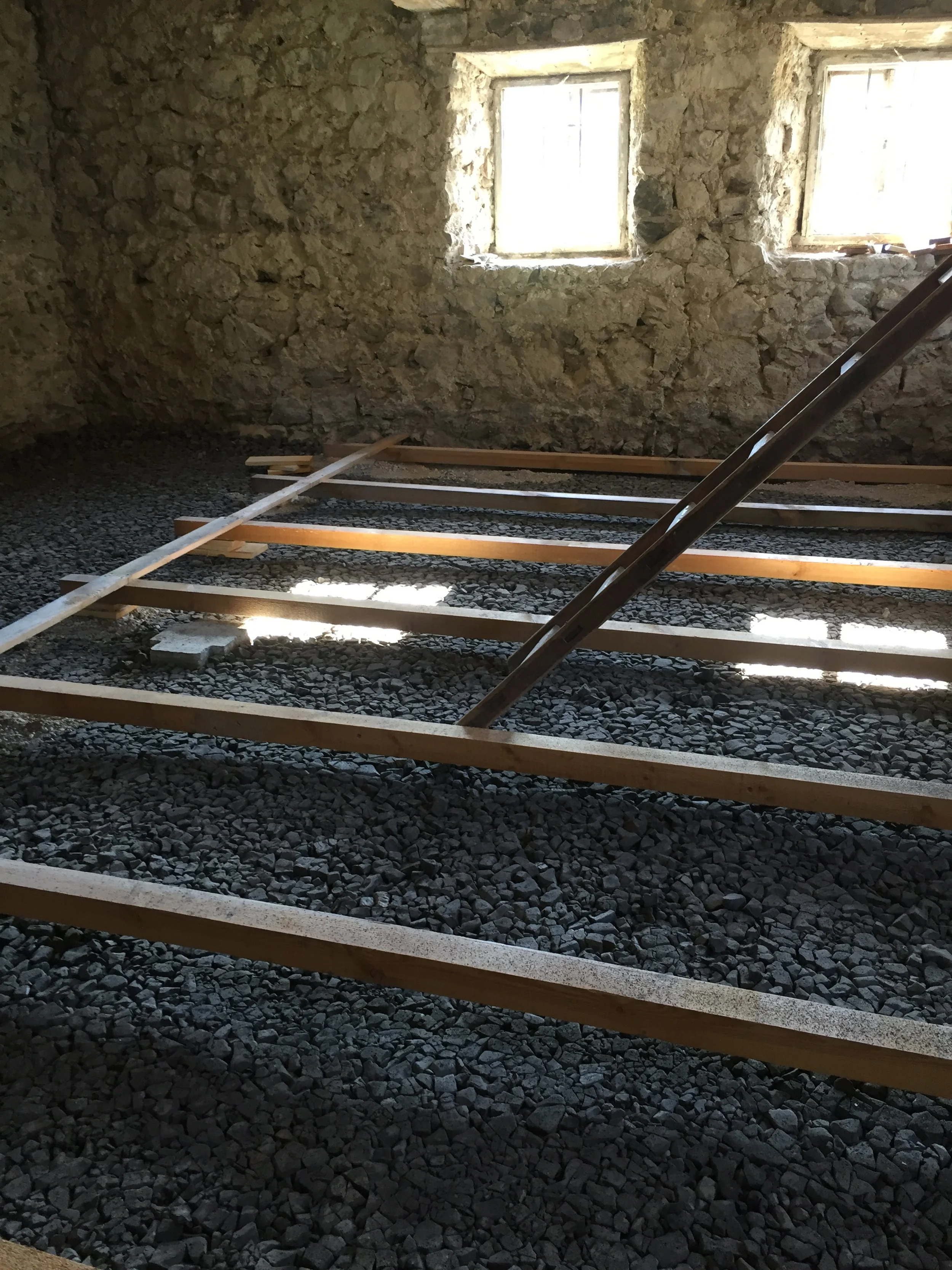 Innenansicht eines raum unter Renovierung mit unbefestigtem Boden und Holzrahmen für den zukünftigen Boden, zwei kleine Fenster in einer Steinmauer