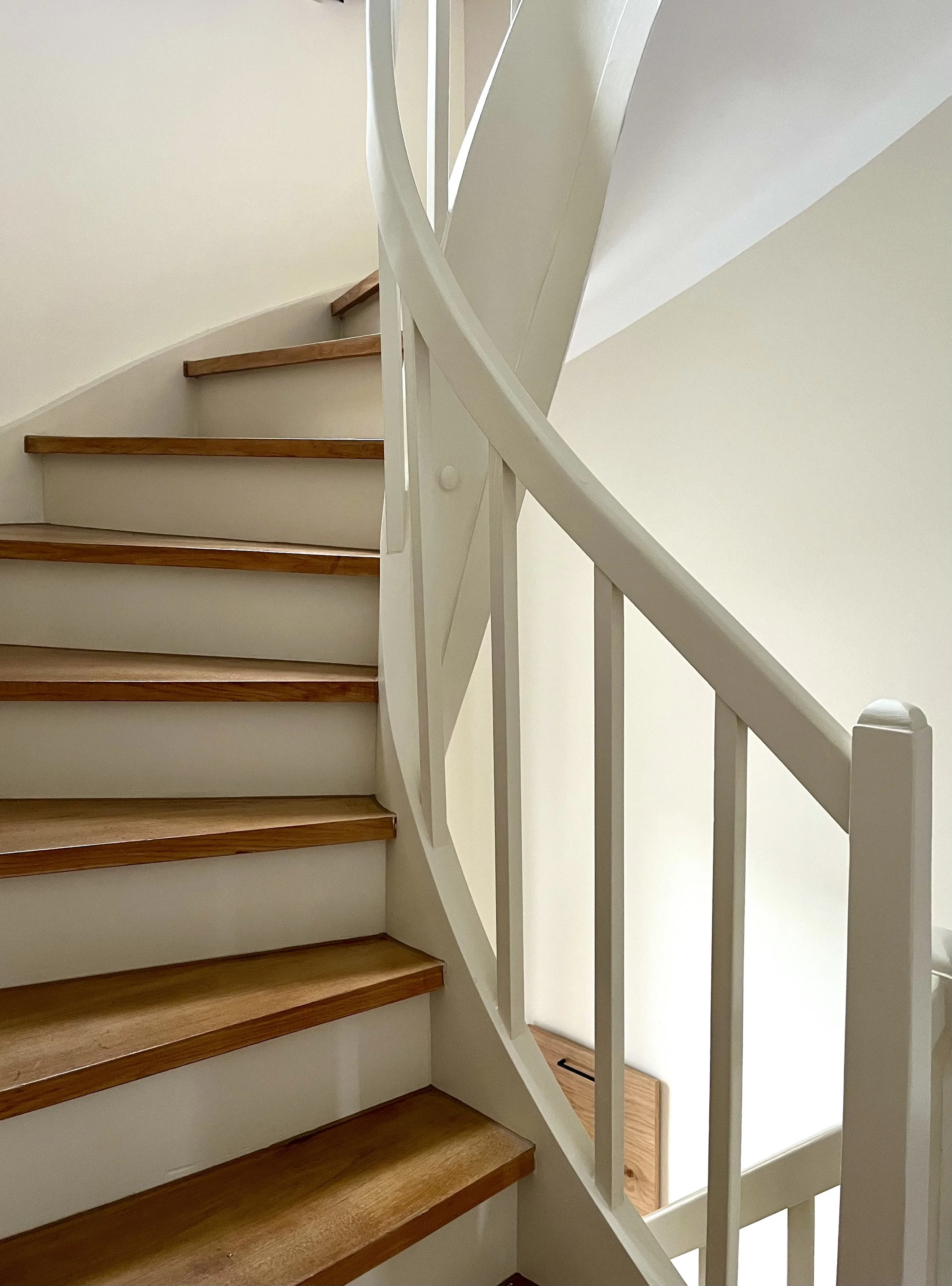Innenaufnahme einer Holztreppe mit weißem Geländer, die sich nach oben windet.