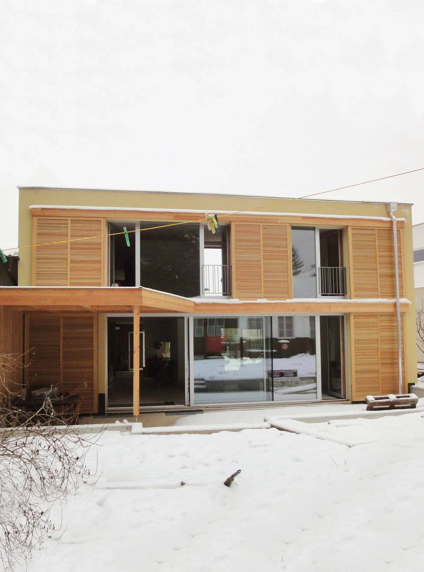 Ein modernes zweistöckiges Haus mit Holzelementen im Winter, Schneebedeckter Garten, offene Türen und Fenster, Außentexturen aus Holz und Glas.