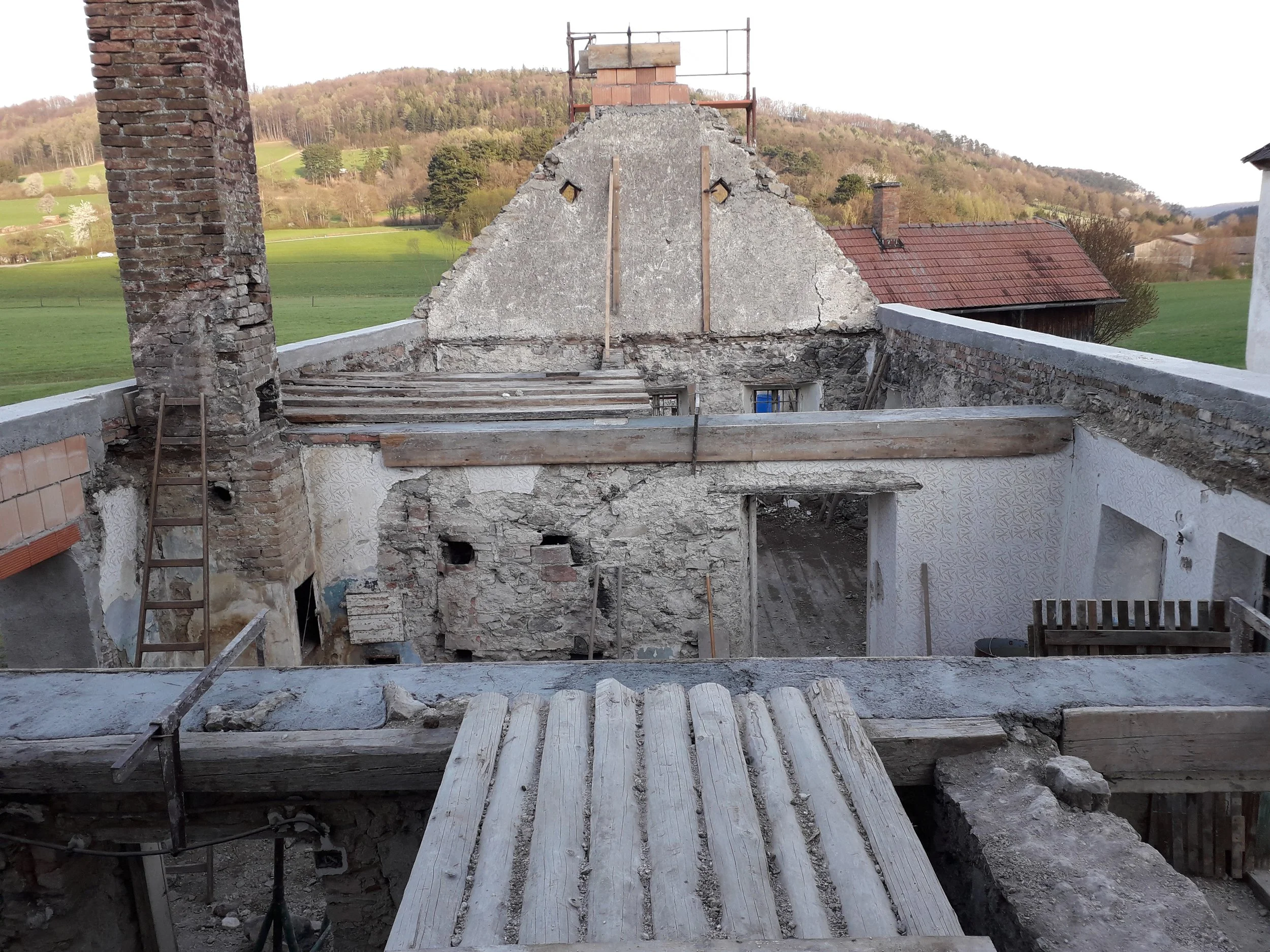 Steinhaus ohne Dach mit offenen Decken - befindet sich im Bau, im ländlichen Gebiet mit Wiesen und Bäumen im Hintergrund.