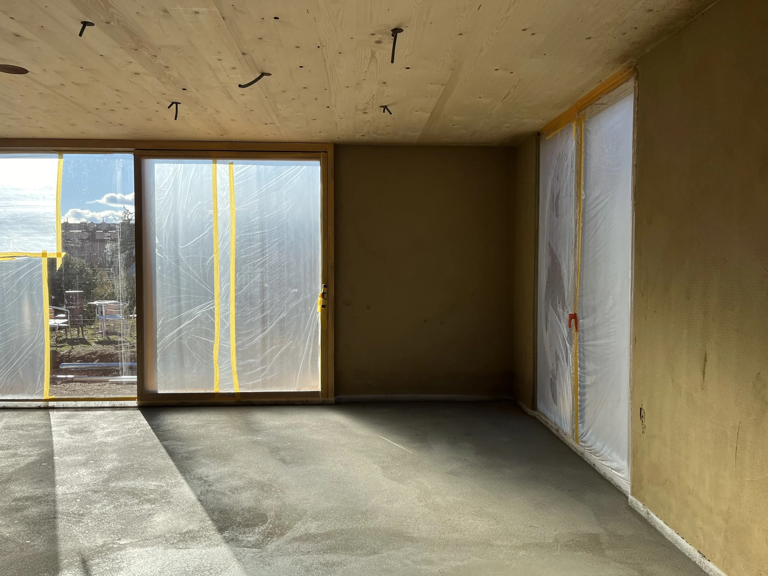 Innenraum eines unreifen, noch im Bau befindlichen Hauses mit großen Fenstern, Holzdecke und Lehmputz.