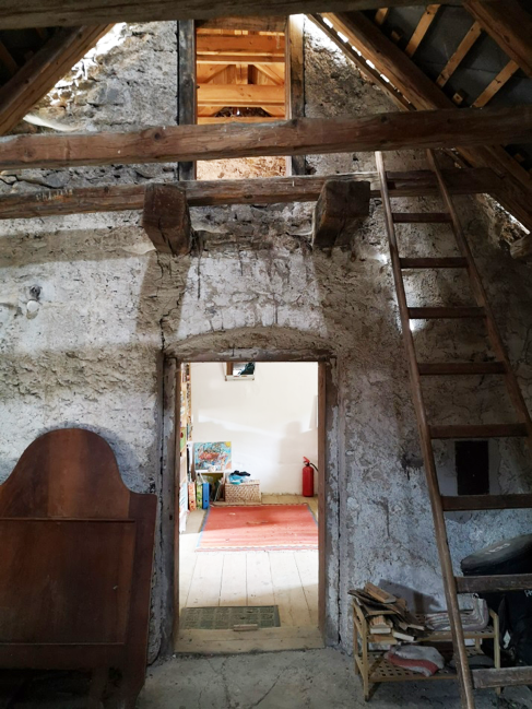 Innenaufnahme eines alten, rustic Hauses mit einer offenen Dachkonstruktion und einer Leiter, die zu einem Zwischenboden führt.