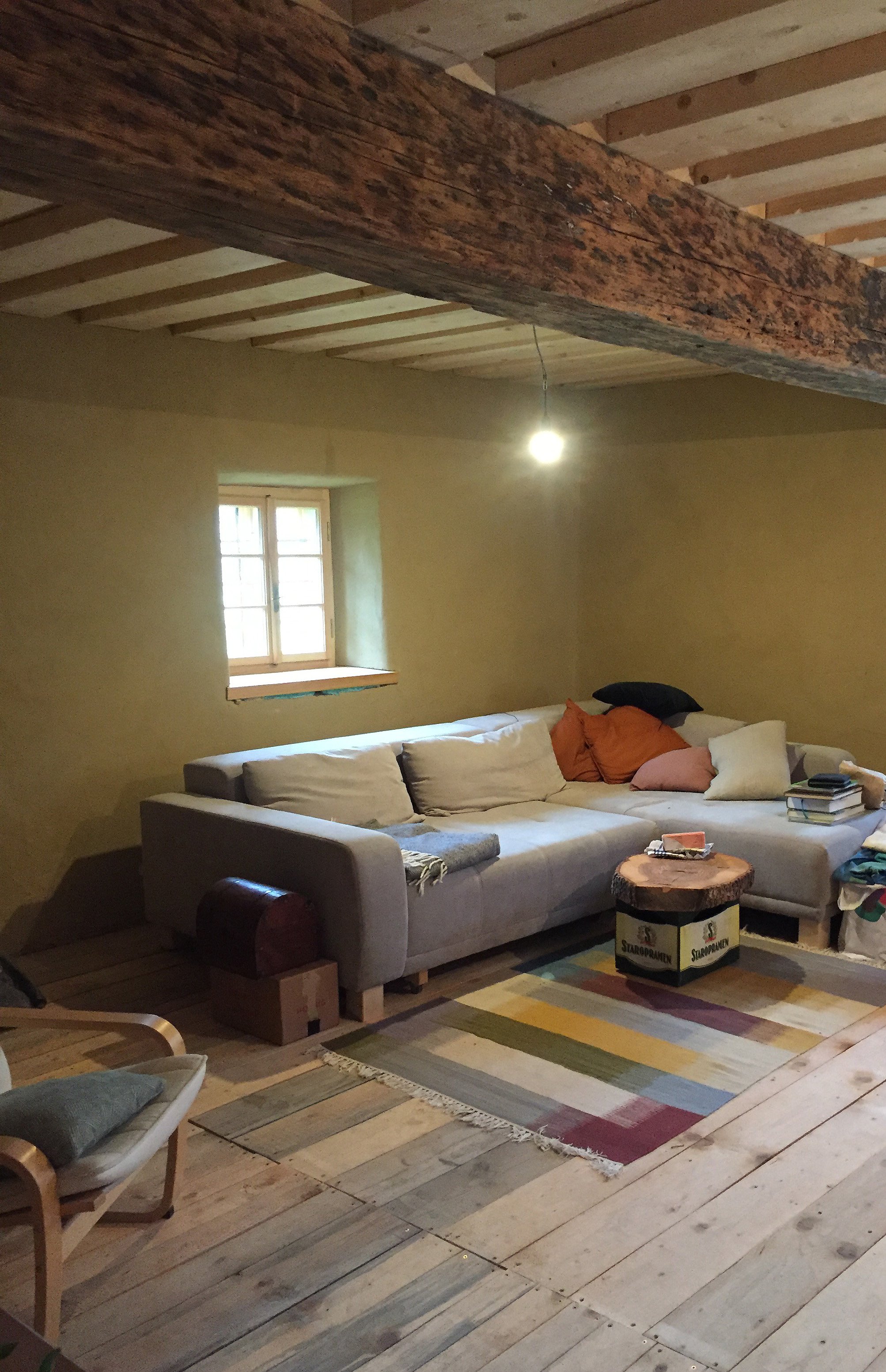 Gemütliches Wohnzimmer mit Sofa, Kissen, Teppich und rustikalem Holzdeckenbalken.