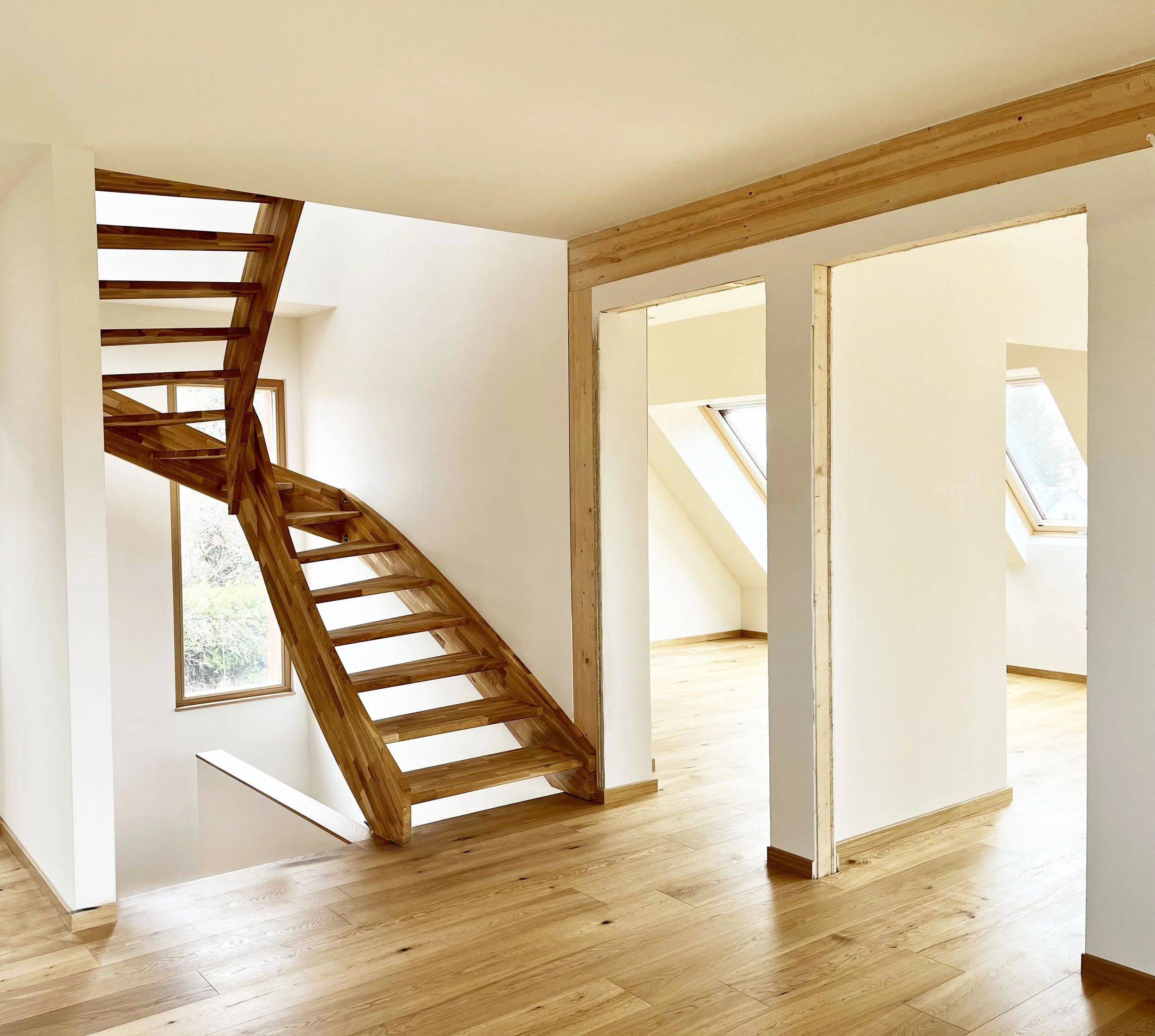 Innenansicht eines noch unfertigen Hauses mit sichtbarer Holztreppe, Terrassenböden und unvollendeten Türrahmen, natürliche Beleuchtung durch Fenster und Dachfenster.