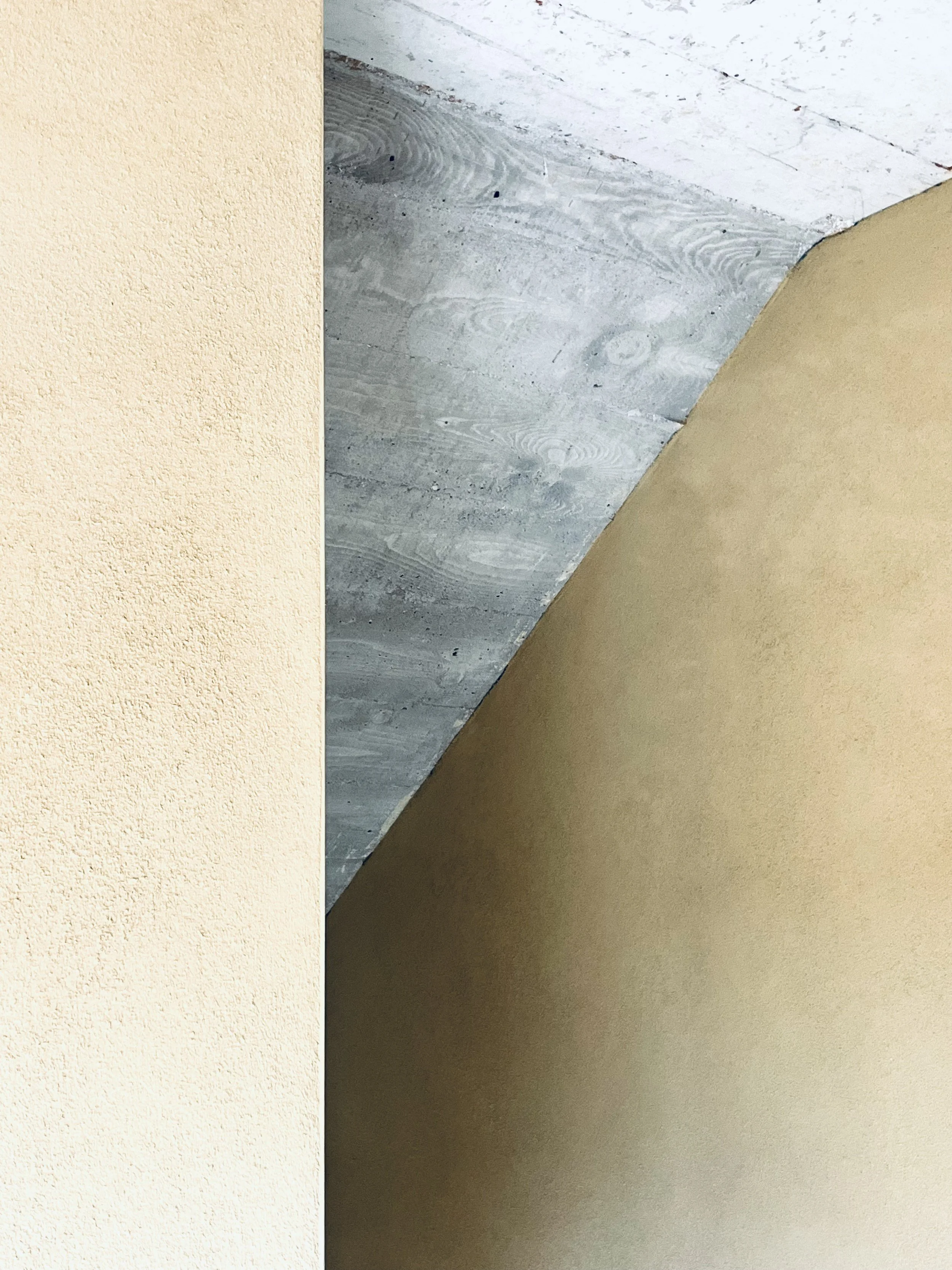 Ein Blick auf eine Sichtbeton Zimmerdecke und Stiegenuntersicht mit unterschiedlichen Texturen und Farben, darunter eine Lehmwand.