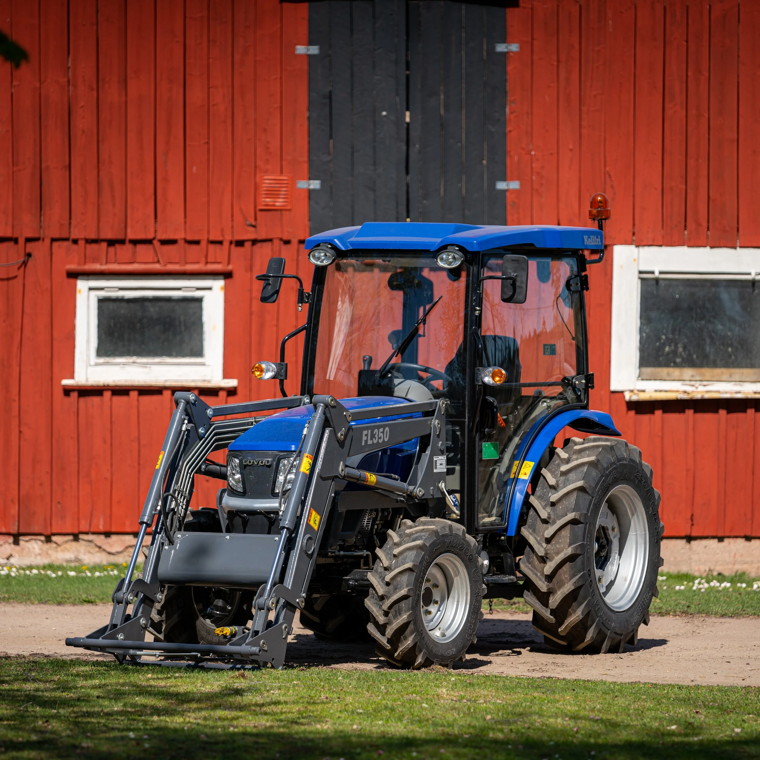 A blue tractor with a front loader attachment parked in front of a red barn.