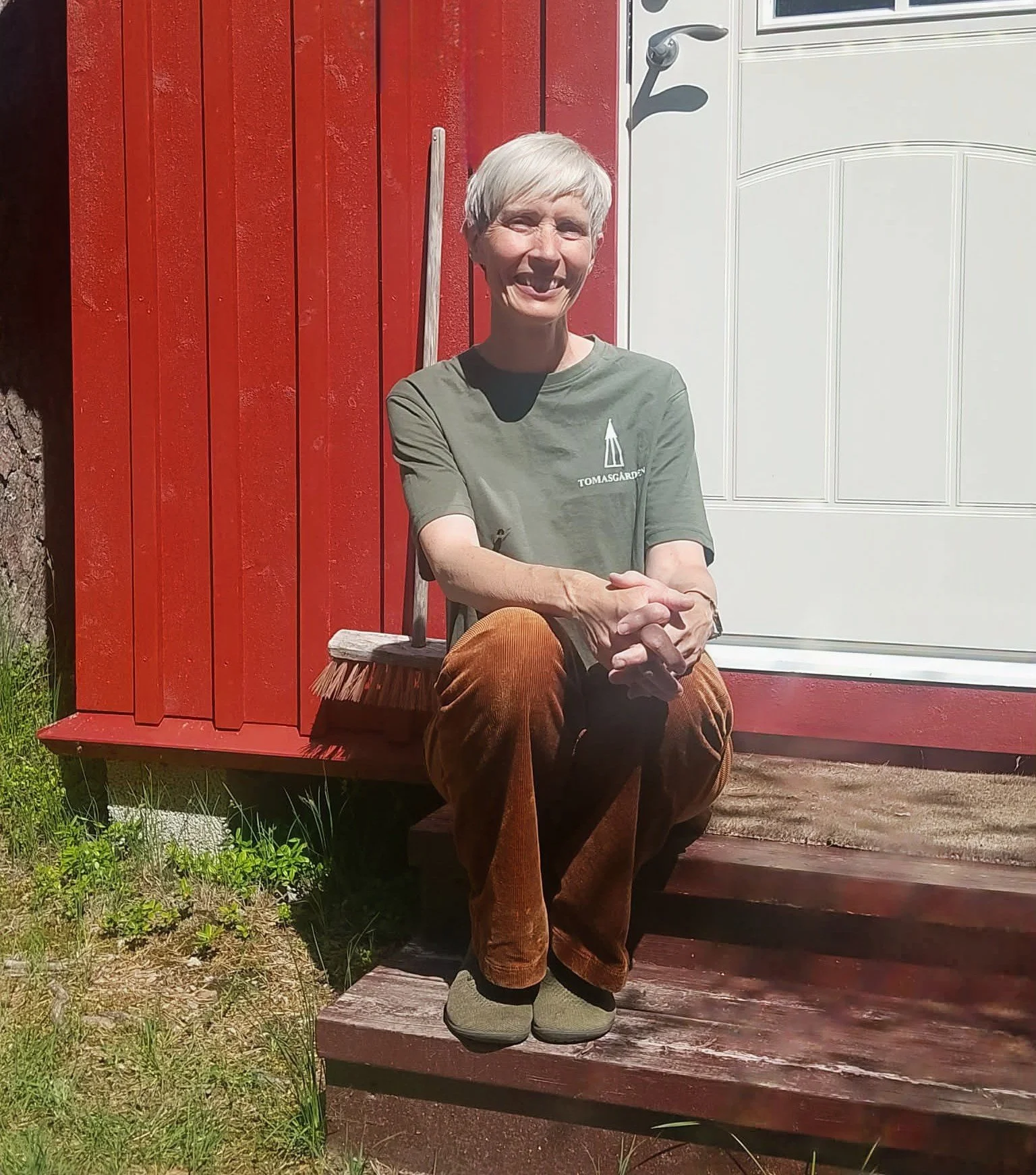 En kvinne sitter på en trapp foran et rødt hus