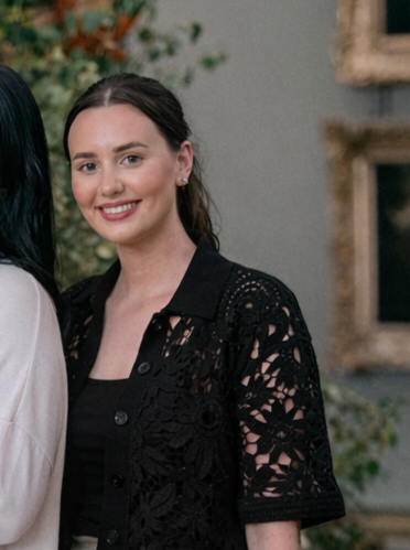 Young woman smiling, wearing a black lace top, standing indoors.