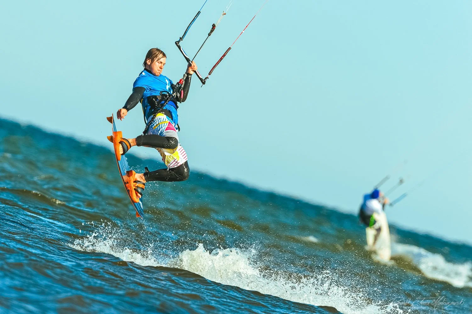 Kiteboarder jumping over the water during a windy day with another kiteboarder in the background.