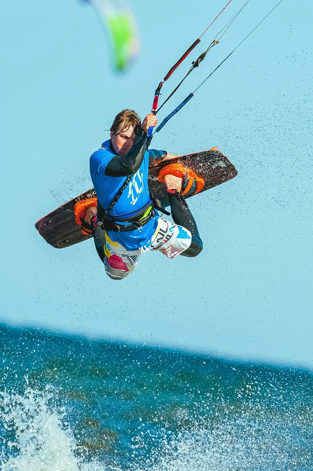 Male kiteboarder performing a jump above the water with a blue sky background.