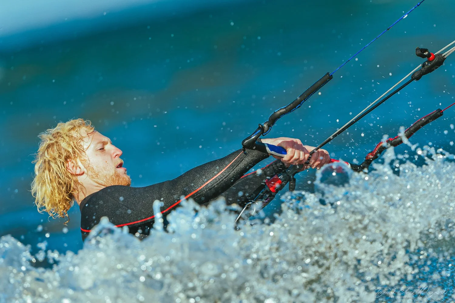 A person with long blonde curly hair is kiteboarding on the water.