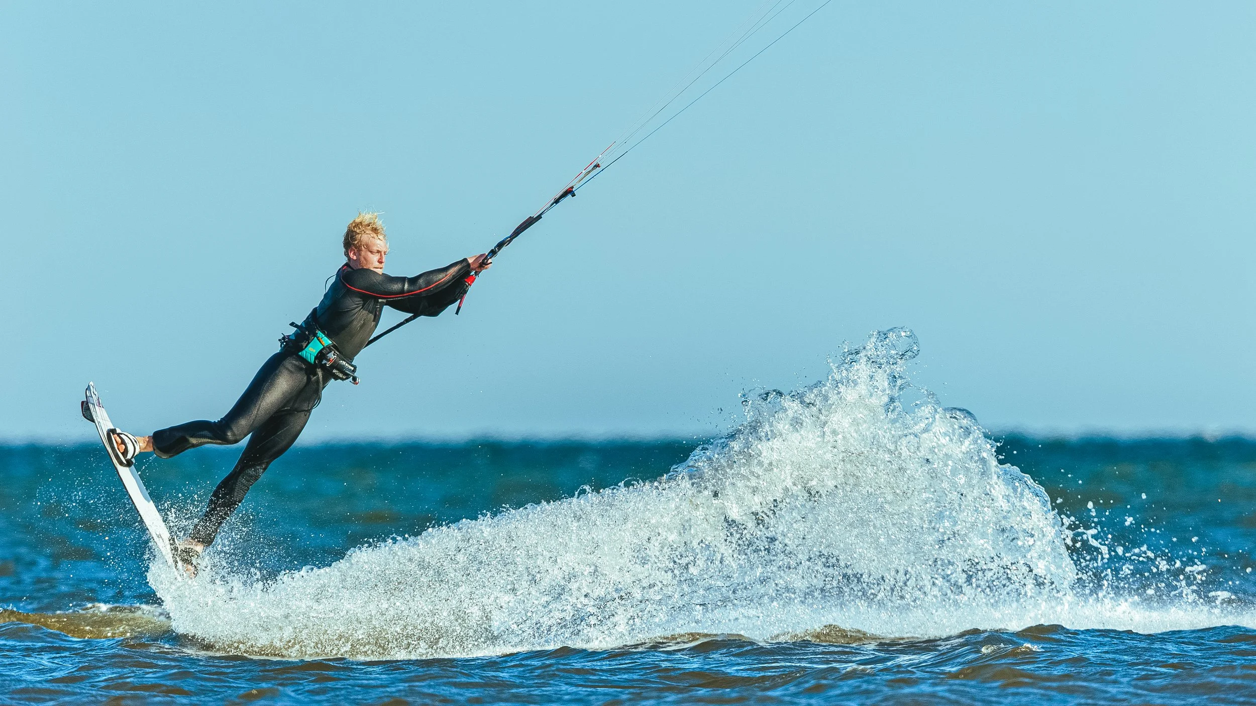 Person kite surfing on the ocean waves under a clear blue sky.