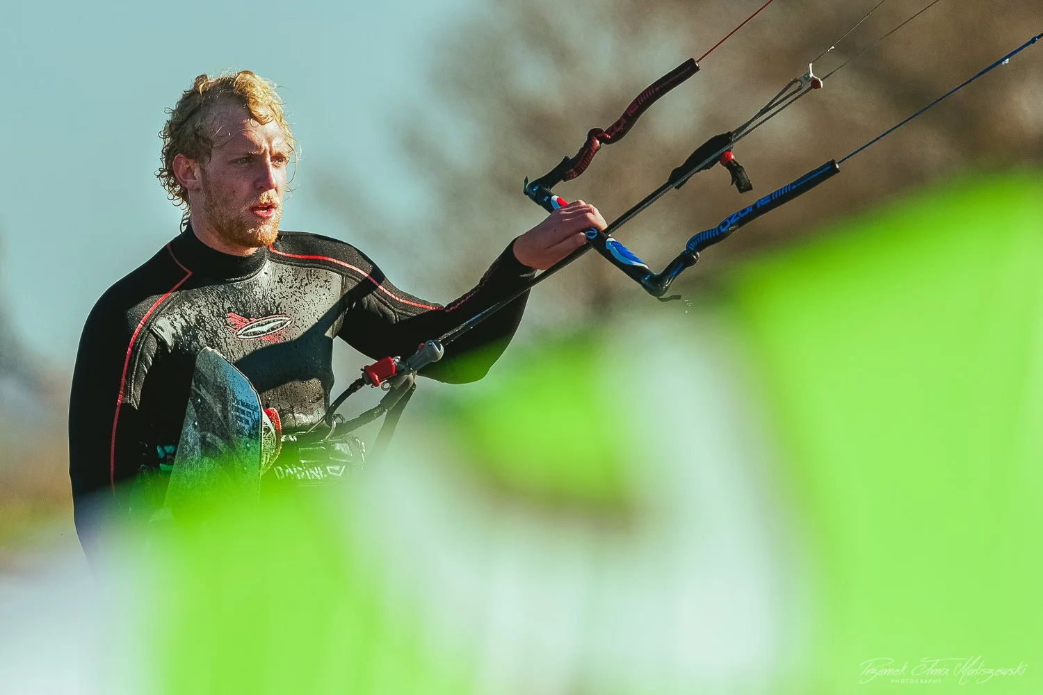 A man in a black wetsuit holding a kiteboarding control bar, preparing to kiteboard on the water.