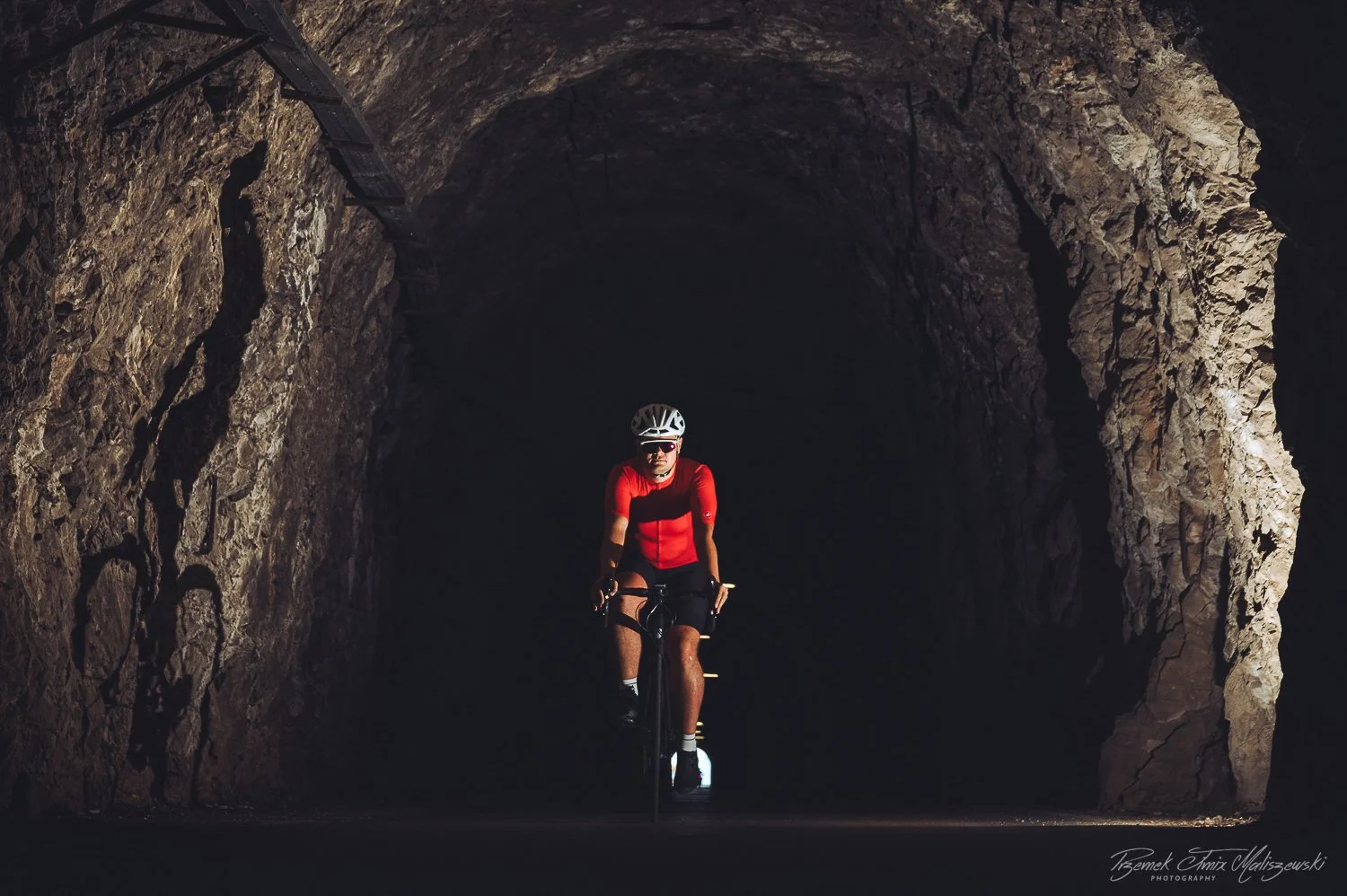 Cyclist riding a bike through a dark tunnel with rocky walls.