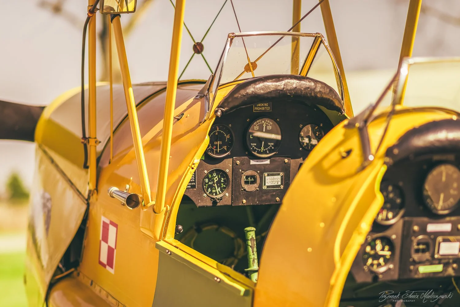 Close-up of the cockpit of a vintage yellow biplane aircraft, showing the instrument panel with various gauges and controls, and part of the open canopy.