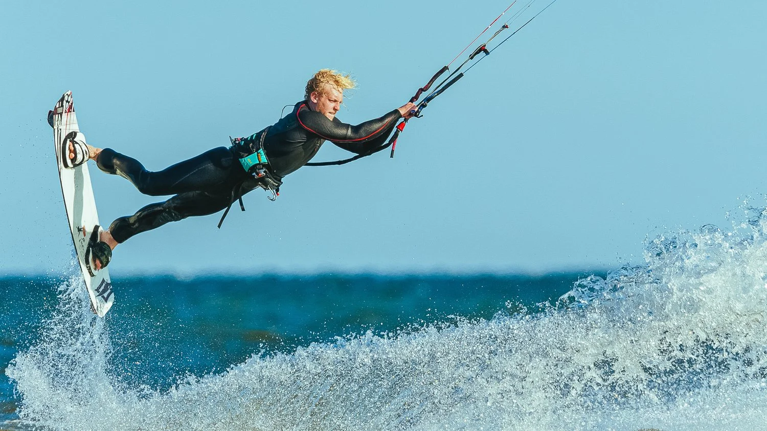 A person wearing a wetsuit kiteboarding on the water, holding onto a kite control bar while lifted above the waves.