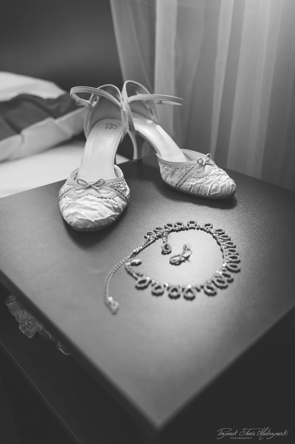 A pair of elegant high-heeled shoes and a necklace with a bow design placed on a table.