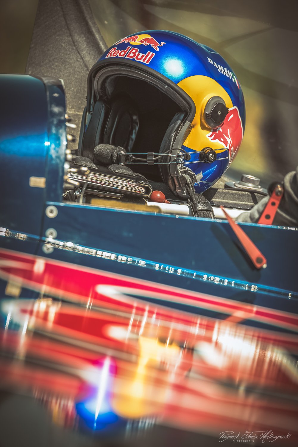 A racing helmet with Red Bull branding and a detailed design, placed on a race car dashboard.