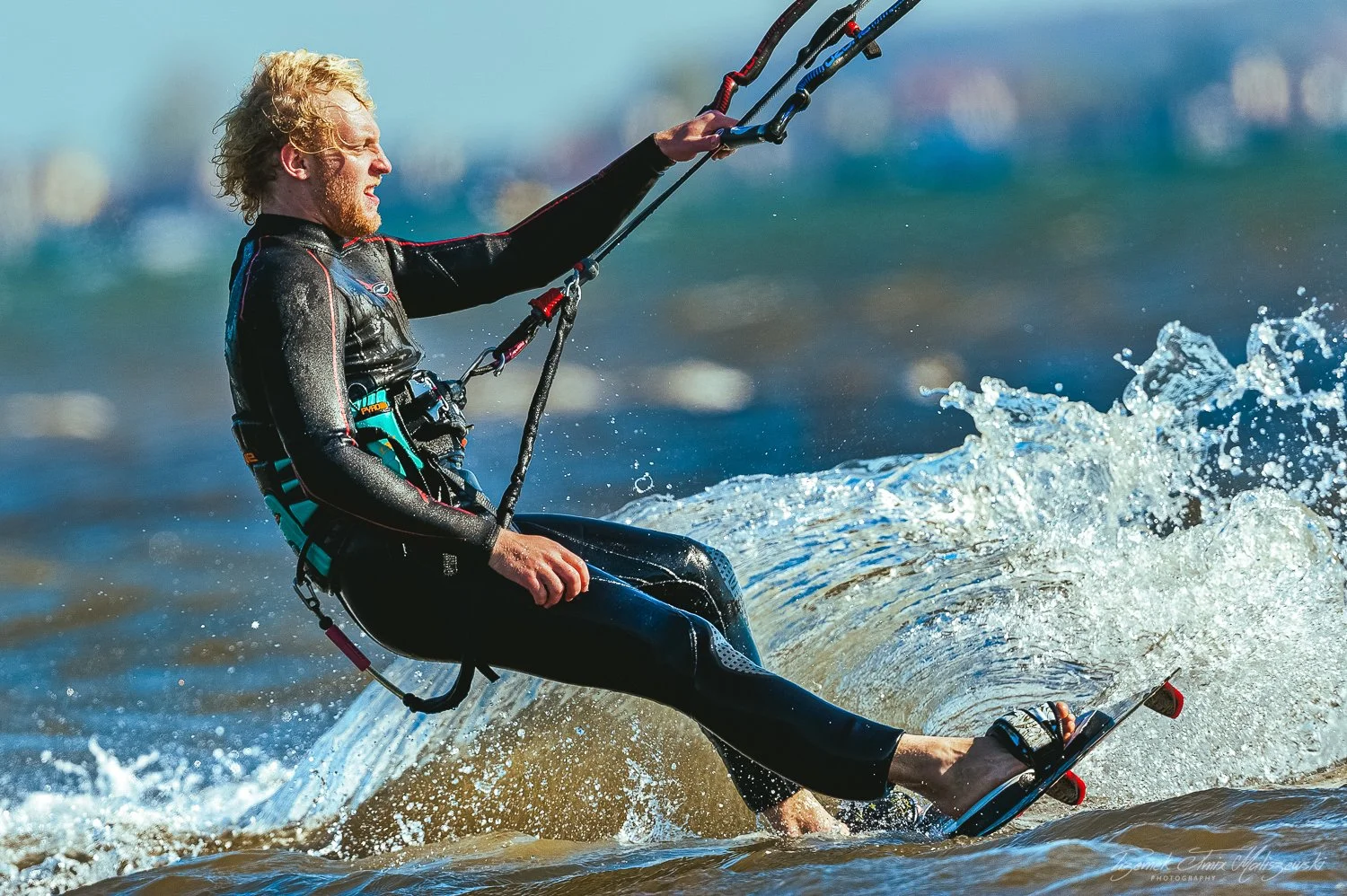 Man kiteboarding on the water with a kite, wearing a wetsuit, and holding the kite control bar.